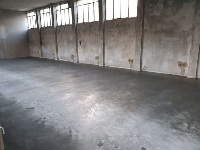 Empty industrial warehouse interior with concrete floor, weathered walls, and barred windows along the side